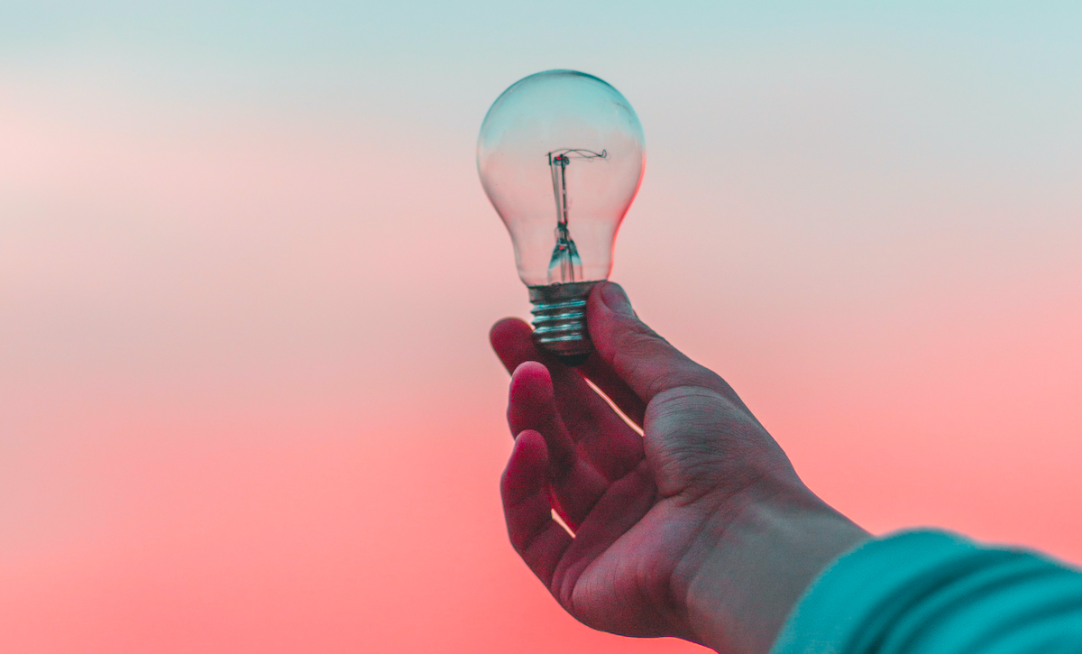 Hand holding light bulb in front of blurry pink and blue background
