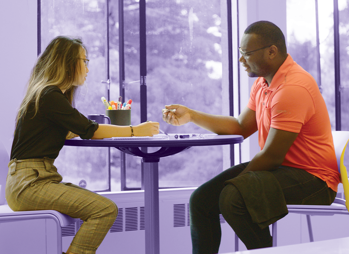 Two students sitting in HCDE's Design Lab look down at a whiteboard table top