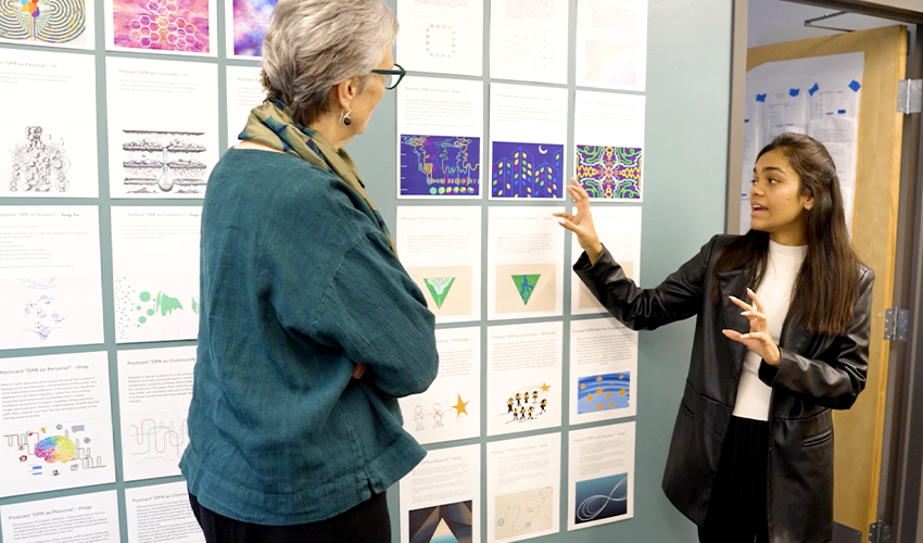 A student points to work hanging on a wall
