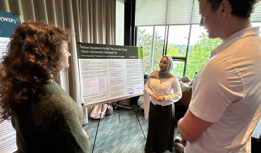 A student stands with their poster at an HCDE research showcase