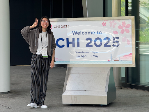 Xiaoyi holds up a peace sign in front of the CHI 2025 sign