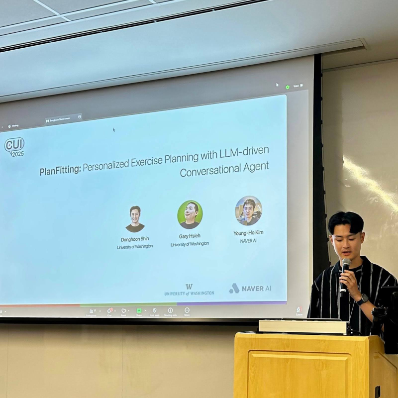 Donghoon stands behind a podium on stage presenting at CUI