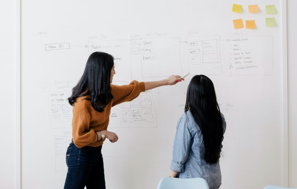 two people stand in front of a whiteboard with wireframe sketches