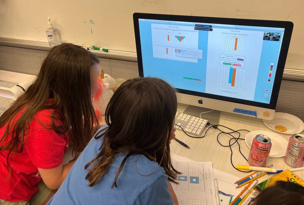 Two children sit together at a desktop computer playing the AI Puzzlers game.