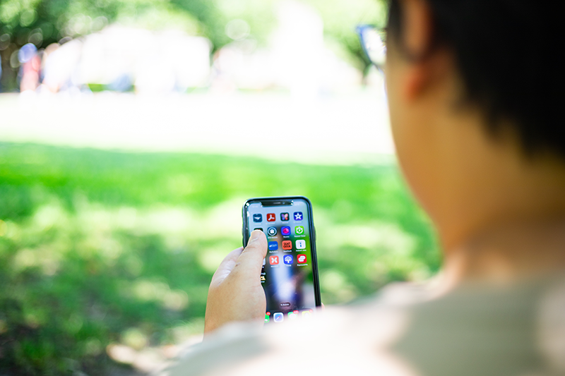 Person sitting outdoors on grass using a smartphone, with app icons visible on the screen.