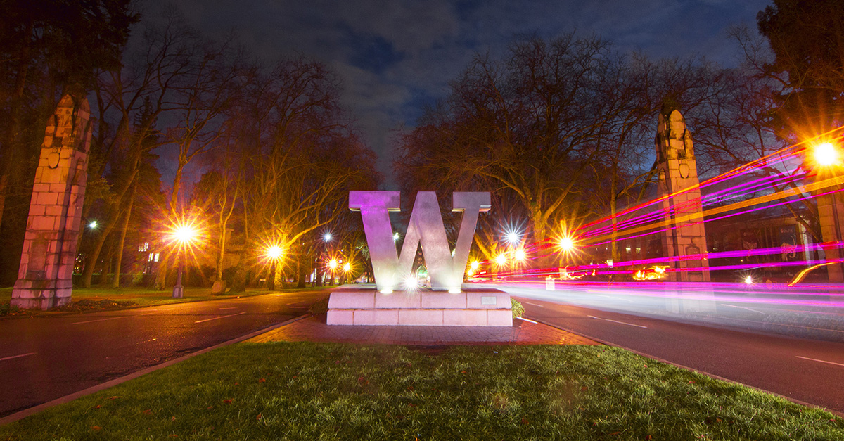 Bronze W sculpture at the UW campus illuminated by streetlights with light trails from passing cars.