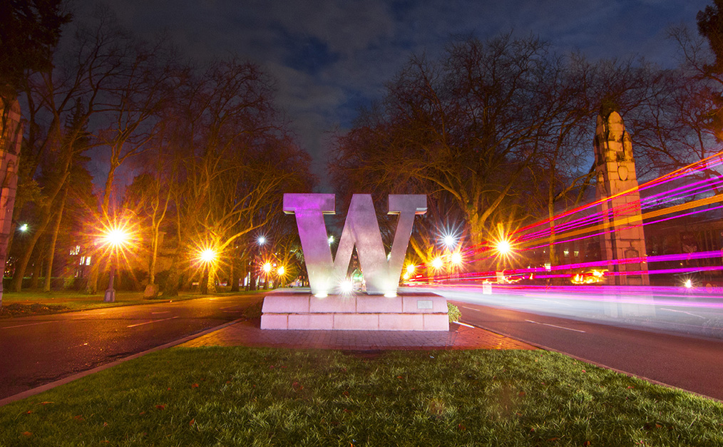 Bronze W sculpture at the UW campus illuminated by streetlights with light trails from passing cars.