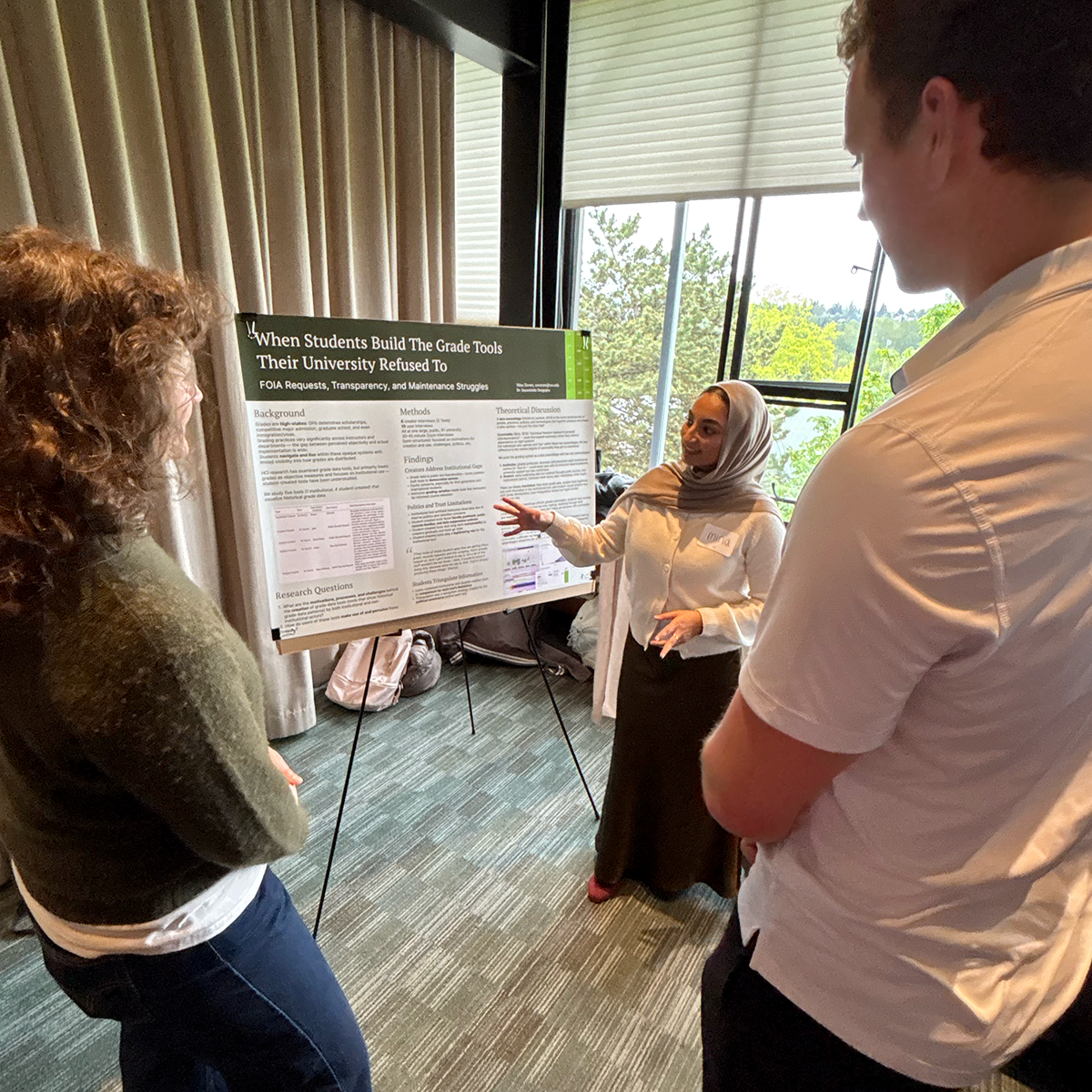 A student stands with their poster talking to attendees