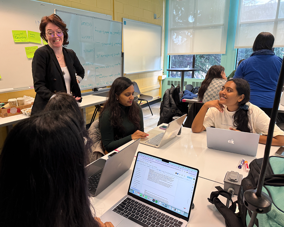A mentor speaks to a table of 3 students in the HCDE Design Lab classroom