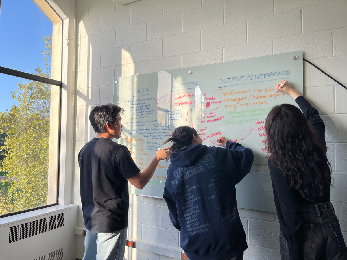 Three students write together on a whiteboard in HCDE's Sieg Building