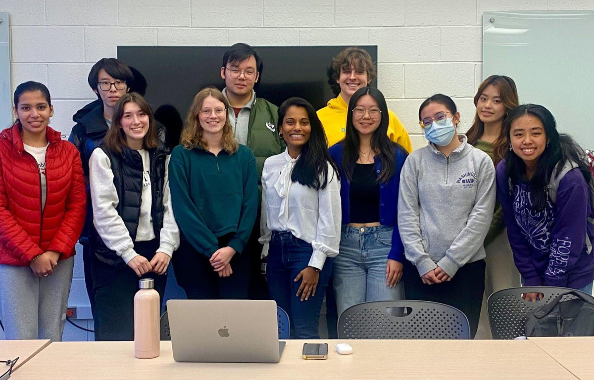Katya stands with a group of students smiling at the camera in an HCDE classroom