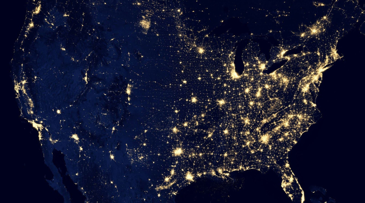 Satellite image of the United States at night, showing concentrated clusters of city lights