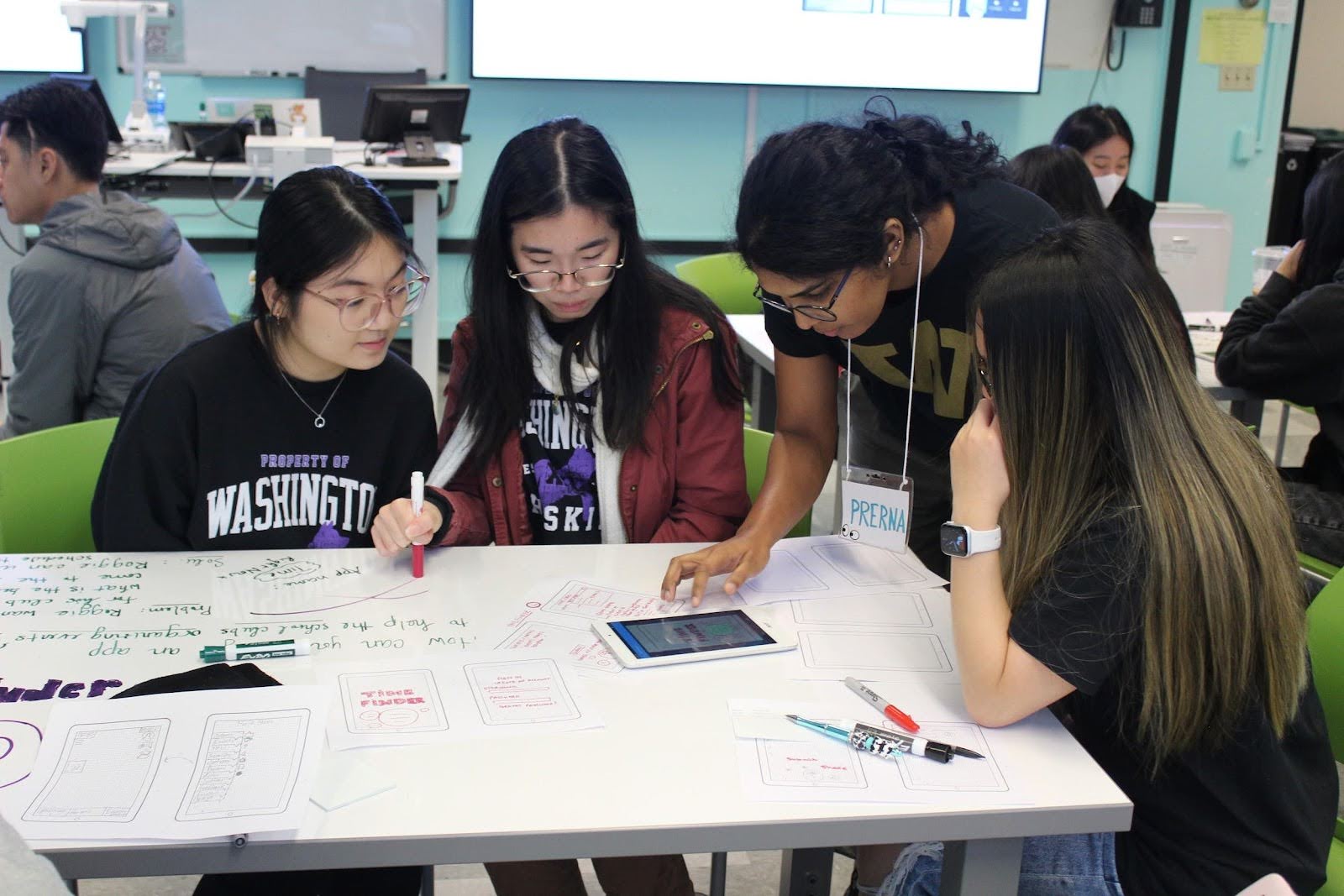 A UW student leans over three seated students collaborating on a whiteboard table in HCDE's Sieg Building