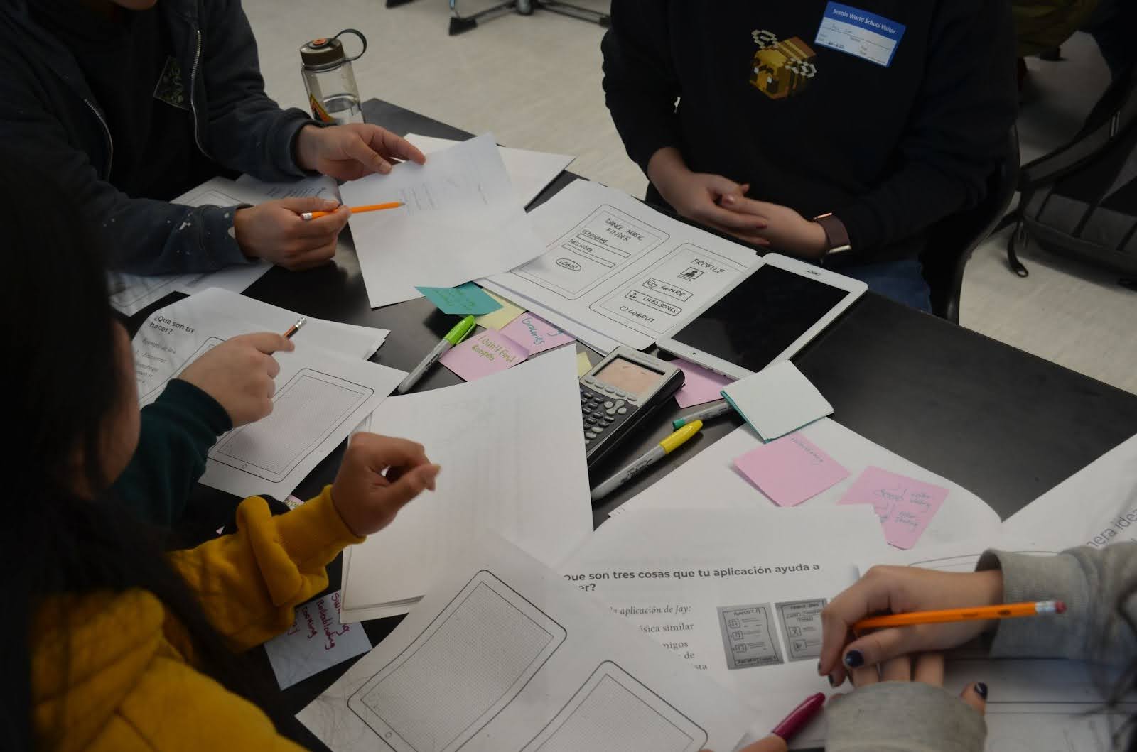 close-up of table with sketches, a tablet, a calculator, and other design tools during a workshop