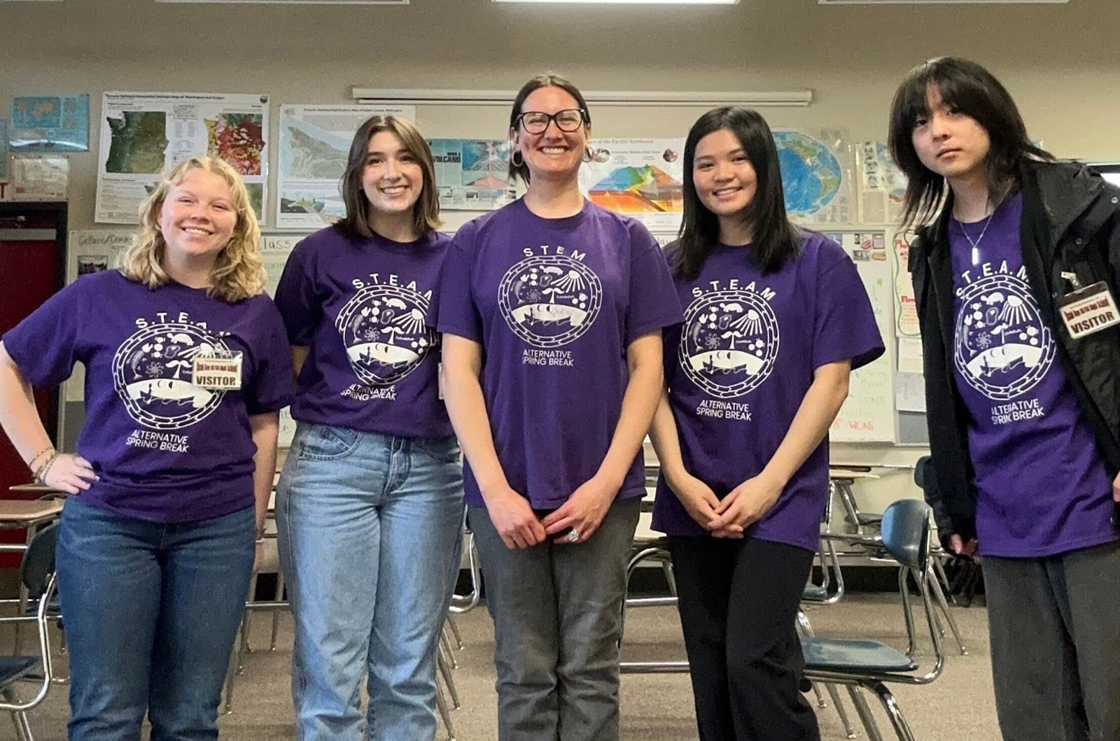Four HCDE students and a teacher pose in Alternative Spring Break t-shirts in a classroom
