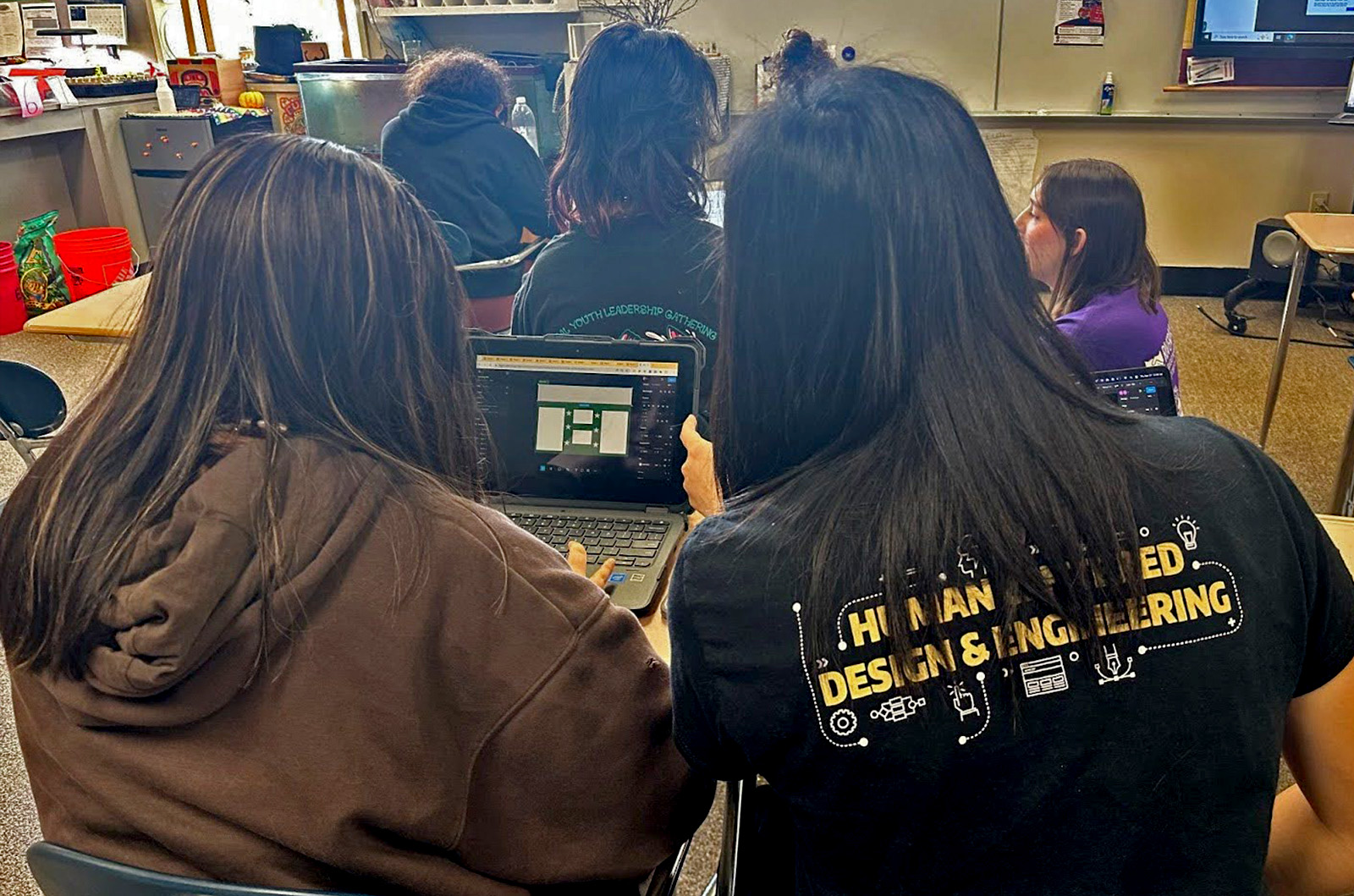 Photo from behind a HCDE student helping a younger student work on a computer