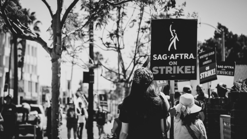 black and white image of 2023 film workers strike with sign visible: "SAG AFTRA on STRIKE"