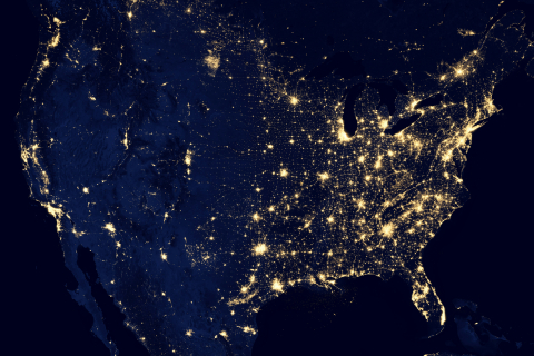 Satellite image of the United States at night, showing concentrated clusters of city lights