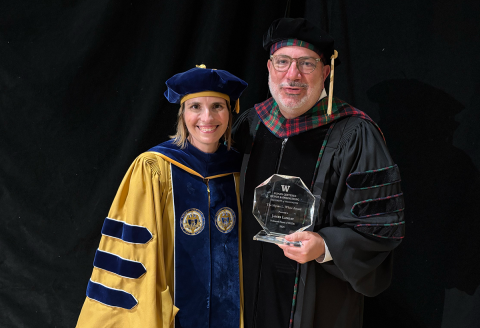 James Landay and Julie Kientz, both wearing regalia, pose with the glass Mikey Award at the HCDE Graduation Ceremnony