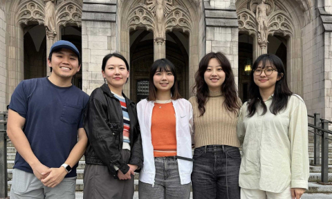 Five students standing side by side smile at the camera in front of a UW building