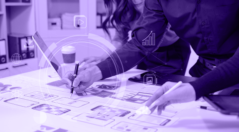 Two people reviewing wireframes and interface sketches spread across a table.