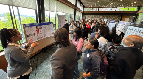 A student presents their poster to a gathering of attendees