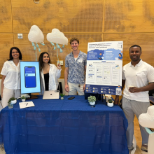 Four HCDE students stand behind a table with their capstone poster 