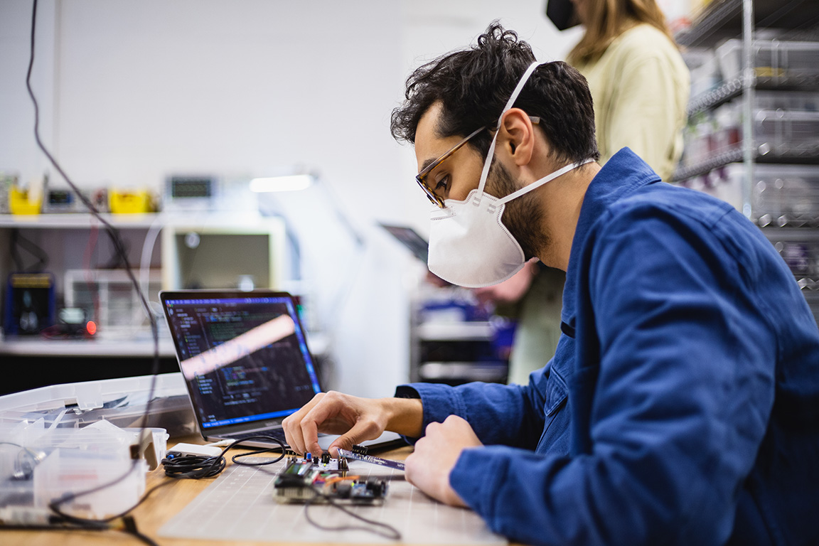 A student adjusting a circuit board hooked up to a laptop