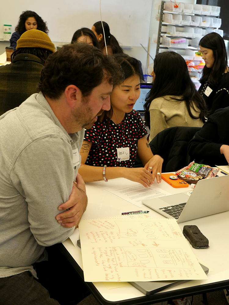 Design Jam mentor and HCDE student speaking while looking at sketches and a laptop