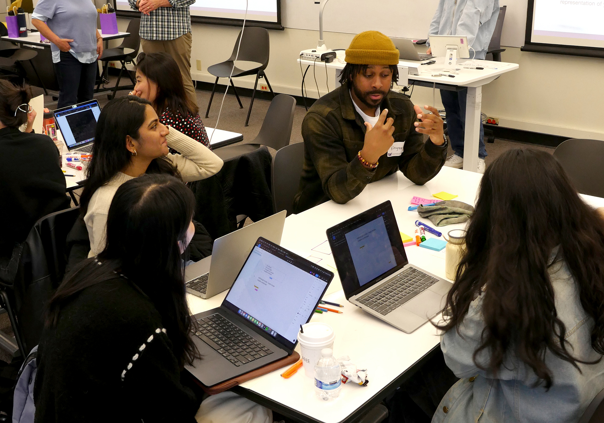 Mentor speaking with team of four students around a table