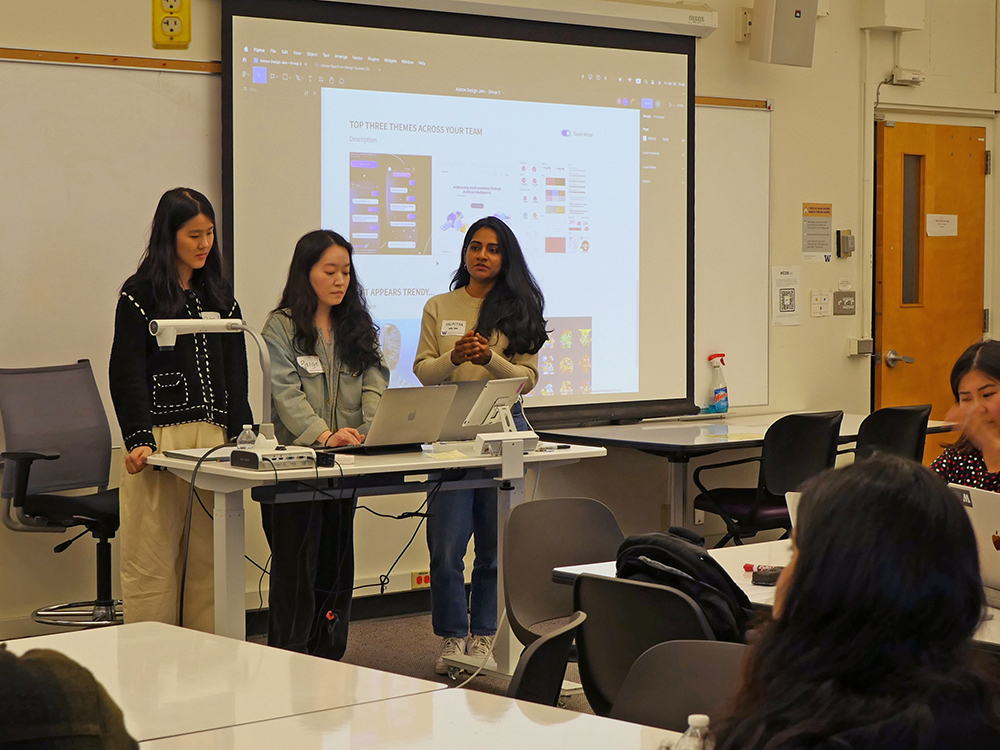 Team of three students presenting their prototype. The screen behind the students says top three themes across your team