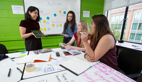 Four students around a table in Sieg Student Lounge. Students are writing on the whiteboard table and all looking at an ipad interface